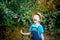 A happy boy six years old in blue clothes and a hat stands in a garden with Apple trees and laughs