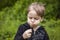 A happy boy on a spring day in the garden blows on white dandelions, fluff flies off him. The concept of outdoor recreation in