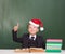 Happy boy in a suit and with red santa hat points on empty green chalkboard