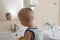 Happy boy taking bath in kitchen sink. Child playing with foam and soap bubbles in sunny bathroom with window. Little baby bathing