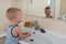 Happy boy taking bath in kitchen sink. Child playing with foam and soap bubbles in sunny bathroom with window. Little baby bathing