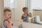 Happy boy taking bath in kitchen sink. Child playing with foam and soap bubbles in sunny bathroom with window. Little baby bathing