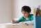 Happy boy using pencil drawing or sketching on paper, Portrait  kid siting on table doing homework, Child enjoy art and craft