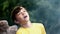 Happy boy in a yellow T-shirt catches raindrops on nature. Smoke from the fire at a picnic. Hike, tourism and family