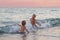 A happy boys are playing in the waves on the beach. Cheerful boys bathes in the sea waves at sunset