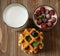 Happy breakfast. A small mug with blueberries, a glass of milk and granola with raspberries.