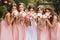 Happy bride with bridesmaid hold bouquets and have fun outside. Beautiful bridesmaid in same dresses stand by the