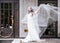 Happy bride covered with flying veil standing on street