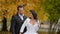 happy bride in embrace of her beloved groom in wedding day, posing outdoors in autumn day