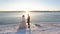 Happy bride and groom bathe in rays of setting sun on coast of river in winter.