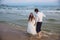 Happy bride and groom run along ocean shore. Newlyweds having fun at wedding day on tropical beach