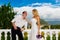 Happy bride and groom standing next to the stone gazebo amid beautiful tropical landscape. Sea, sky, flowering plants and palm tr