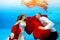 Happy bride and groom swim underwater at sunset. They look at each other and smile with a red cloth in their hands on a blue