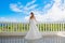 Happy bride standing next to the stone gazebo amid beautiful tropical landscape. Sea, sky, flowering plants and palm trees in