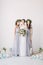 Happy bride in a white dress holds a wedding bouquet and poses with her friends in elegant dresses. White room is