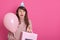 Happy brunette girl with pink balloon and bithday present in hands, keeps mouth opened, being in surprise, looks aside with