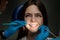 Happy brunette woman patient examined by dentist in blue gloves using dental instruments sitting in dental chair under the lamp in