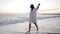 Happy brunette young slim barefoot woman strolling on sandy Mediterranean sea beach in slow motion at sunset. Wide shot