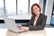 Happy business woman with red hair smiling at work typing on computer laptop at modern office desk