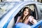 Happy businesslady in dark red shirt driving her car and showing thumb up. Smiling lady taking steering wheel of her new car.