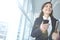 Happy businesswoman using her phone and carrying files at work. One female businessperson browsing online using social