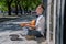 Happy busker street musician sitting on a city sidewalk and playing music with guitar. Freedom, music and art concept