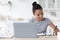 Happy busy teen afro american girl studying at table with laptop, in kitchen interior