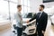 Happy buyer of car shaking hands with seller in auto dealership, in front of car