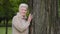 Happy calm mature middle aged single woman looking at camera posing near large tree, smiling older female, healthy