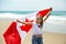 Happy Canadian girl carries fluttering white red flag of Canada against blue sky and ocean background.