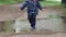 Happy carefree child runs through a puddle in raincoat and blue rubber boots