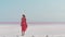 Happy carefree elegant woman in blowing pink dress enjoys her vacation while walking along white salty beach with