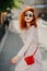 Happy carefree redhead woman laughs positively, spends free time outdoor in city, wears sunglasses, long sleeved dress, carries