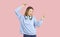 Happy carefree teen girl with headphones on her neck having fun dancing on light pink background.