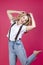 Happy Caucasian Blond Girl in Casual White Shirt With Suspenders Posing With Lifted Hand in Motion Against Coral Background