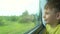 Happy Caucasian boy looks out the train window at nature. Travel by train during summer holidays. The child enjoys the vastness ou