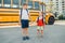 Happy Caucasian brothers students with hearing aids by yellow school bus. Smiling kids with disabilities holding hands. Back to