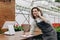 Happy Caucasian businessman talking on cellphone while standing in apron in small floral center and writing down order details.