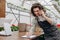 Happy Caucasian businessman talking on cellphone while standing in apron in small floral center and writing down order details.