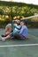 Happy caucasian couple sitting on outdoor tennis court by net embracing after playing tennis