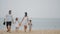 Happy Caucasian family, father, mother and two kids walking together smiling, holding hands along amazing ocean beach.