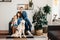 Happy caucasian family mother, father and daughter sitting at home near in living room decorated by trees in pots with their big