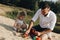 Happy caucasian family in white dress, dad playing with little girl with sand toys playing in sandbox at summer