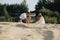 Happy caucasian family in white dress, mother and dad playing with little girl with sand toys playing in sandbox at