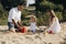 Happy caucasian family in white dress, mother and dad playing with little girl with sand toys playing in sandbox at