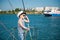 Happy caucasian little boy in white captain hat and striped tank top with denim shorts standing on luxury yacht board adjusting