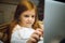 Happy caucasian little girl during video call or messaging with Santa using laptop and home devices, looks delighted and