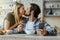 Happy caucasian millennial blonde wife kisses husband with stubble, guy have lunch, holds smartphone