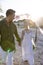 Happy caucasian newlywed couple holding hands and walking at beach at wedding ceremony at sunset