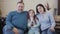 Happy Caucasian parents and daughter watching TV sitting on couch. Joyful relaxed man, woman and girl resting on